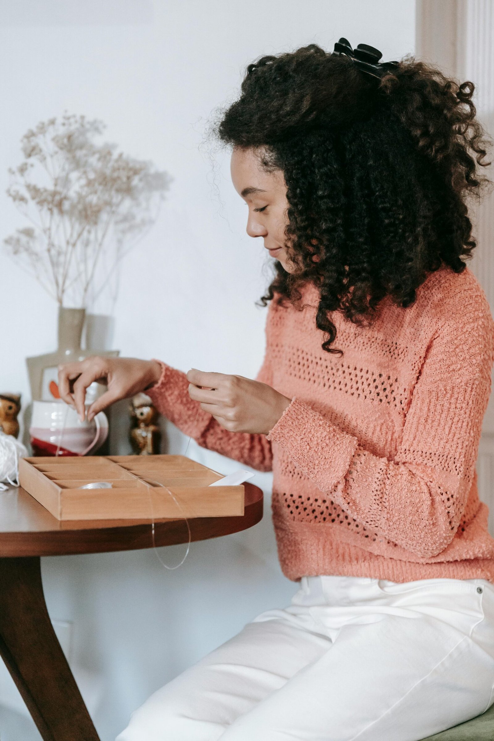 A woman engaged in crafting handmade jewelry with beads and thread at a home setting.